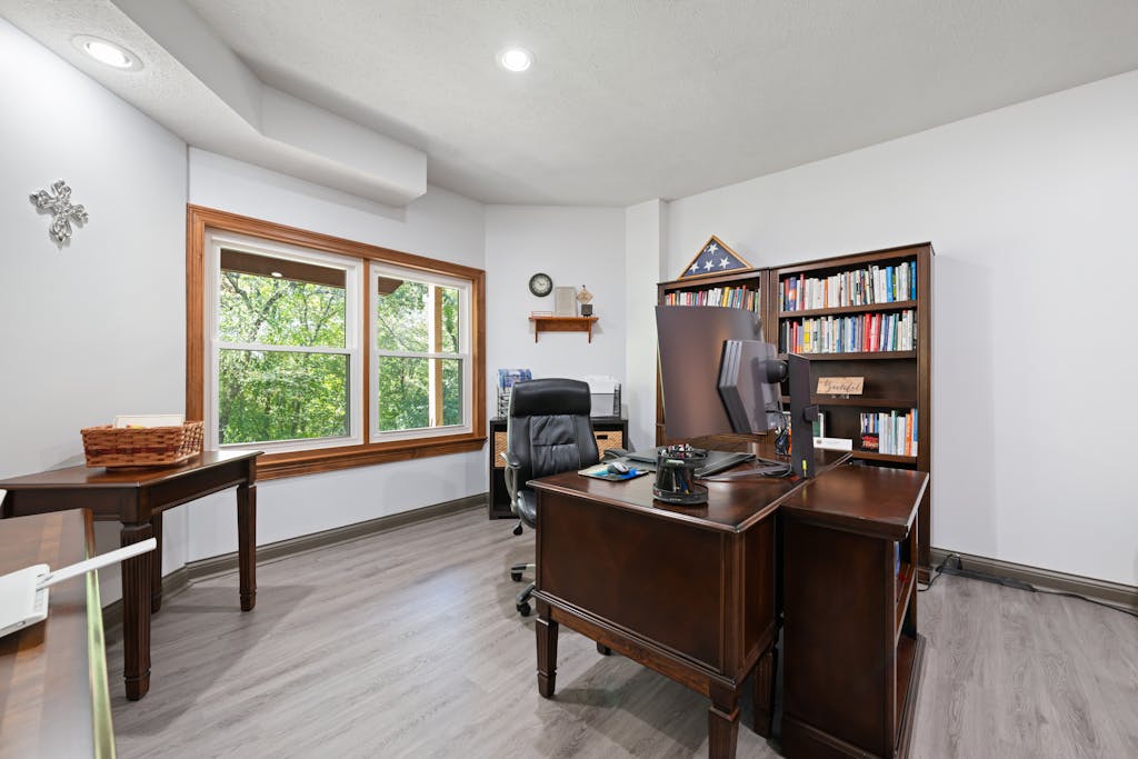 A bright, stylish home office featuring a wooden desk and bookshelves with a view of nature outside.